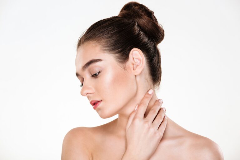 Portrait of gentle young woman with healthy body touching her neck posing over white background with face downwards